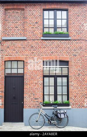 Bruges, Belgium - August 16, 2013: View of the wall with windows, dark door and vintage bike with bag Stock Photo