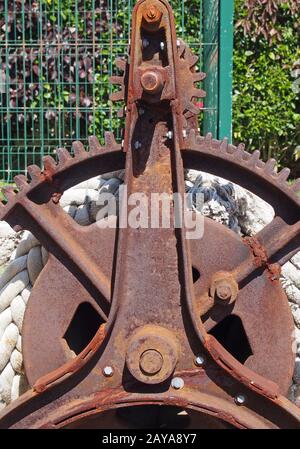 an old disused rusty iron winch with broken cog wheel gears and rope Stock Photo