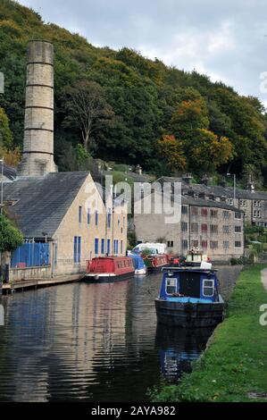 scenic view of hebden bridge with historic buildings along the canal and moored houseboats with towpath and surrounding woodland Stock Photo