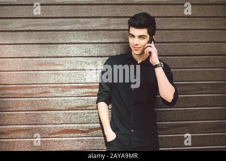 Portrait model young handsome male suspect Turkish middle eastern brunette in black shirt uses hand phone to call technology on Stock Photo