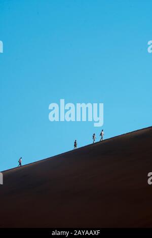 Tourists climbing a dune in the Namibian desert at Dead Vlei Stock ...