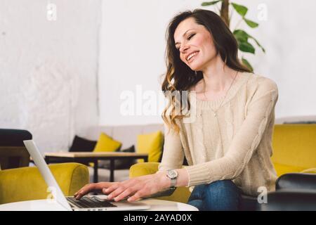 Young middle aged Caucasian woman with long hair. Casual clothes using laptop computer indoors. Cafe restaurant on chair wooden