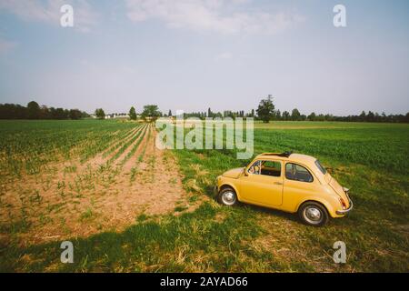 Old retro little yellow car stands in a field in Europe Italy 2013 Stock Photo