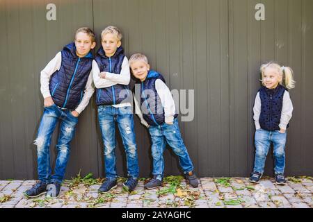 Funny Caucasian big family of three brothers and sister posing standing on growth background of wall in full growth. Equally sty Stock Photo