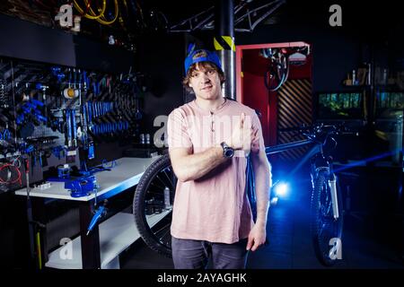 Small business and bicycle transport service. Portrait of a young man in a cap posing against the backdrop of a bicycle workshop Stock Photo