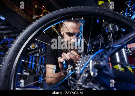 Subject profession. Young stylish caucasian male with a beard at work is repairing a bicycle. Bike shop, service and repair of b Stock Photo