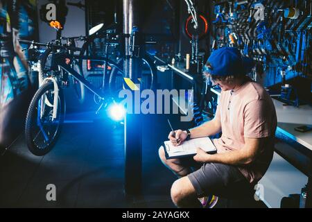 Young handsome stylish man in a cap snapback and with a tattoo small business owner selling a bicycle, the workshop sits on the Stock Photo