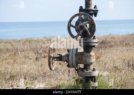 Old rusty weathered aged valve of abandoned pipe system equipment closeup on seashore and blue water Stock Photo