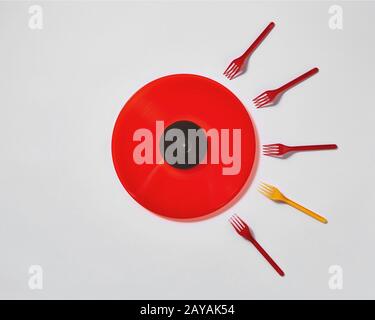 Red vinyl record with plastic colorfut forks on a gray background. Stock Photo