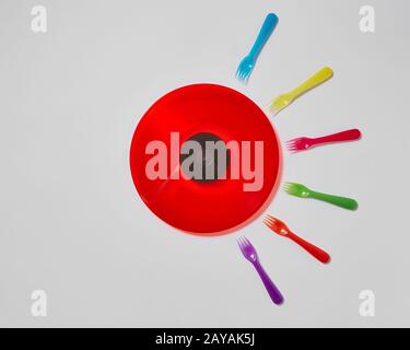 Colorful plastic forks around red vinyl record on a light gray background. Stock Photo