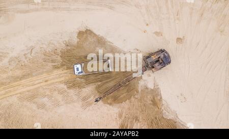 View from above of excavator pours sand into the truck. On the construction site.