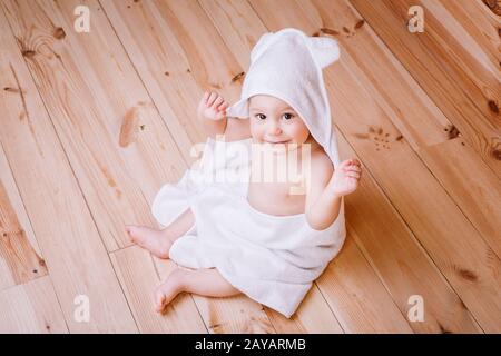 baby boy with brown eyes is five months old wrapped in a white towel with ears on wooden background . Stock Photo