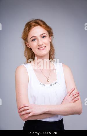 portrait vertical up to the waist young, beautiful business woman, student with lred, curly hair and freckles on gray background Stock Photo