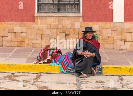Indigenous Tarabuco lady with traditional clothing sitting on the sidewalk by the local market, region around Sucre, Bolivia. Stock Photo