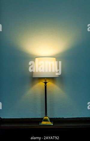Metal base table lamp lighted lying wooden furniture. Luminous stand chandelier classic style. Colored wall background. Contempo Stock Photo