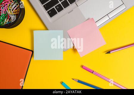 Front view open trendy metallic silver slim laptop blank sticky notes pencils markers clips container notepad colored background Stock Photo