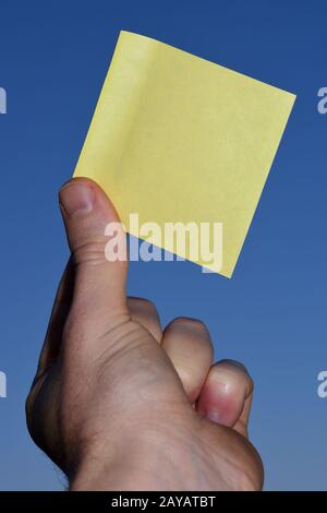 Rectangular yellow note paper held by one hand raising up to the sky. A person hold Piece of square sheet in the sunny day. phot Stock Photo