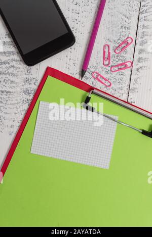 Close up front view colored clipboard blank paper sheet sticky note clips smartphone pencil lying retro old wooden rustic vintag Stock Photo