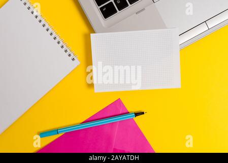 Part view open trendy slim silver metallic laptop highlighter marker squared paper sheet spiral notebook envelope colored backgr Stock Photo