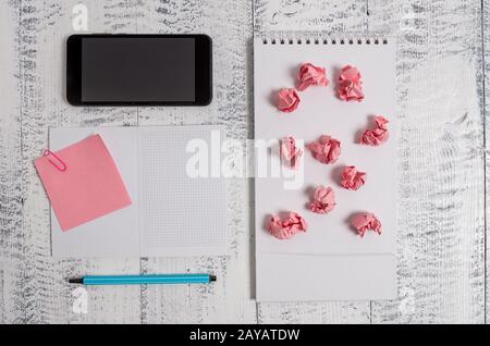 Squared open spiral notebook marker sticky note clip smartphone paper balls lying wooden retro vintage rustic old background. Em Stock Photo