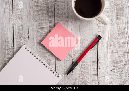 Writing equipments beside cup coffee on the wooden background. Empty paper and stationary placed next to mug of drink above tabl Stock Photo
