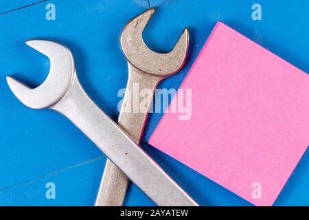 Front view two crossed working wrenches sticky colored notes wooden background. Do it by yourself note. Things repair. Sheet squ Stock Photo