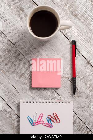 Writing equipments beside cup coffee on the wooden background. Empty paper and stationary placed next to mug of drink above tabl Stock Photo