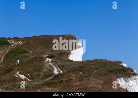 Young couple man woman walking down cliff surface. Two persons standing on rock enjoying summer holidays recreation. Sunny day b Stock Photo