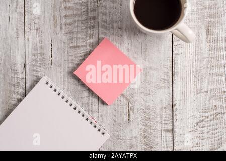 Writing equipments beside cup coffee on the wooden background. Empty paper placed next to mug of drink above table. Artistic way Stock Photo