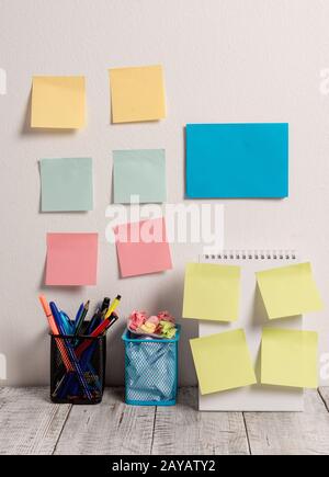 Neat Workplace with Blue Card and 10 Empty Colored Stick Pad Notes Put on Both White Wall and Open Spiral Notebook with 2 Full P Stock Photo