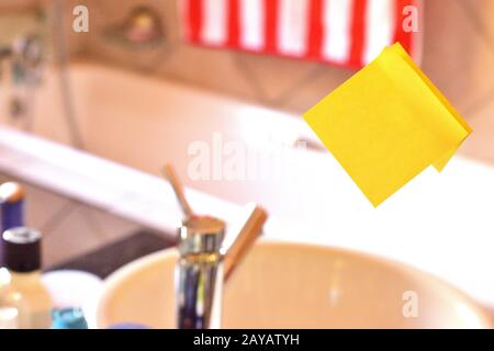 Rectangular yellow note paper attached on toilet mirror. Piece of square sheet use to give notation stick to washroom glass that Stock Photo