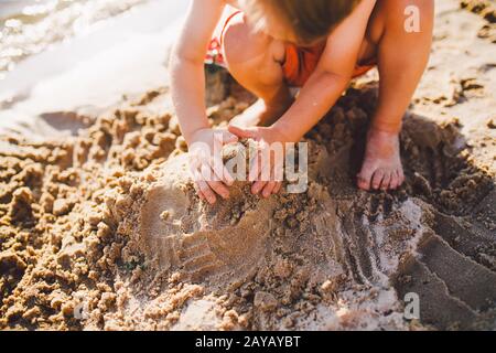a little boy builds figures from the sand on the shore of the pond at sunset of the day, hands dig up the sand in crisp plan
