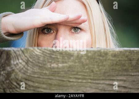 Stalking woman behind a fence hiding her face. Stock Photo
