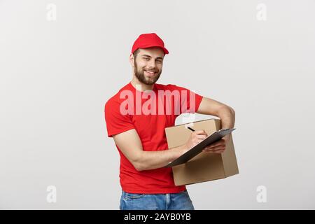 Portrait of smiling male delivery man writing on clipboard and holding box. Isolated over white background Stock Photo
