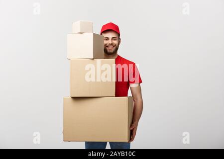 Delivery Concept: Handsome delivery man hold pile cardboard boxes on grey background. Stock Photo