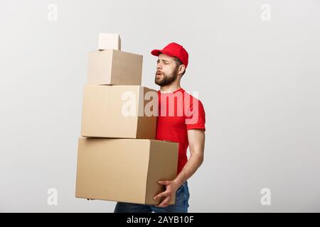 Delivery Concept: Handsome delivery man hold pile cardboard boxes on grey background. Stock Photo