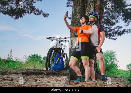 Happy couple with mountain bike taking selfie smartphone outdoors. A happy couple, who lead an active lifestyle, stopped in the Stock Photo
