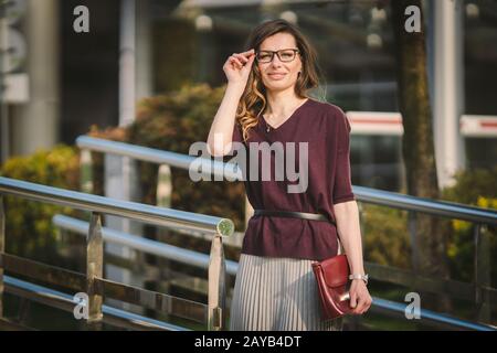 Caucasian adult lady woman in glasses posing near office building outside. Business lady in skirt holds hand glasses for vision Stock Photo