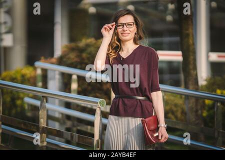 Caucasian adult lady woman in glasses posing near office building outside. Business lady in skirt holds hand glasses for vision Stock Photo