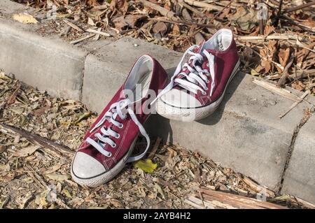 Pair of worn out vintage red old canvas sneakers on outside concrete surface Stock Photo