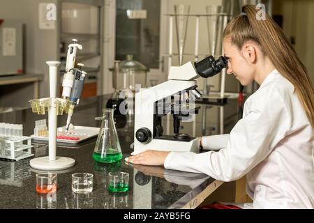 Young female laboratory technician working on compound microscope Stock Photo
