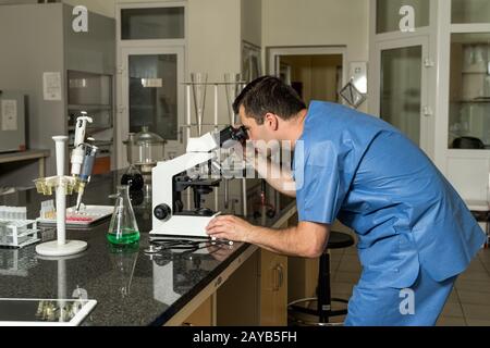 Middle age male laboratory technician working on compound microscope, laboratory equipment and glass Stock Photo