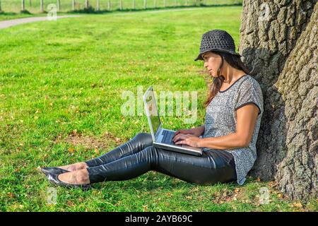 Woman works on laptop at tree in nature Stock Photo