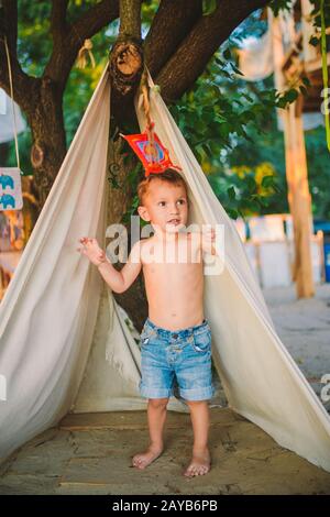 theme summer vacation, little boy, Caucasian child playing in wooded area in park on playground in the yard. The kid in Tipi wig