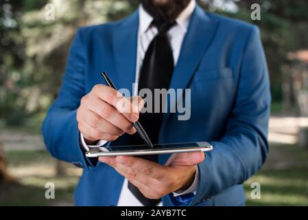 Business concept with man holding mobile phone with touch screen. Businessman holds lap top in his hand. Businessman in blue sui Stock Photo