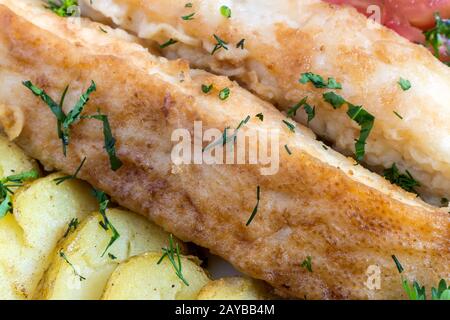 Fried fish with potatoes, vegetables and greens close-up. Stock Photo