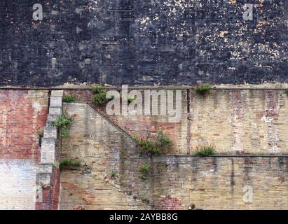 full frame image of a very large old brick wall with many patched and repaired sections stains weeds and black painted area Stock Photo