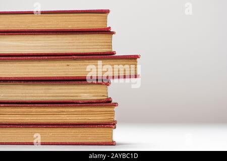 A stack of old red hardcover books with yellow pages on a white grey background. Stock Photo