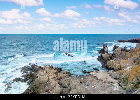 rocky sea shore in the afternoon. blue waves crashing the coast. fluffy clouds above the horizon. Stock Photo