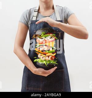 Woman holds a flying homemade burger from fresh organic ingredients on a light background. Stock Photo